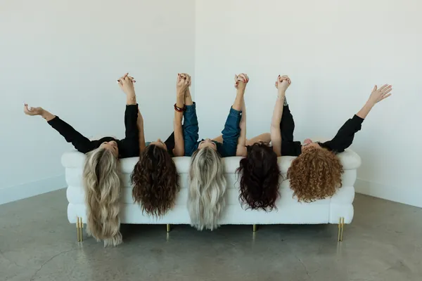 Stylists lying on a white sofa with their hair hanging over the edge and arms raised